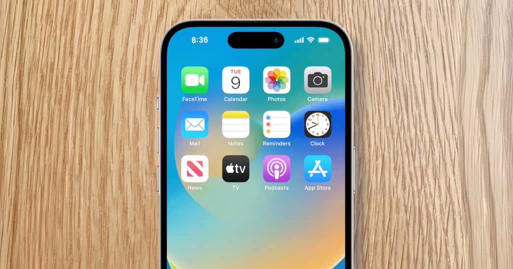 iPhone yang diletakkan di atas meja kayu menampilkan ikon aplikasi utama dan mendemonstrasikan kiat praktis untuk memeriksa model dan kondisi iPhone bekas saat membelinya