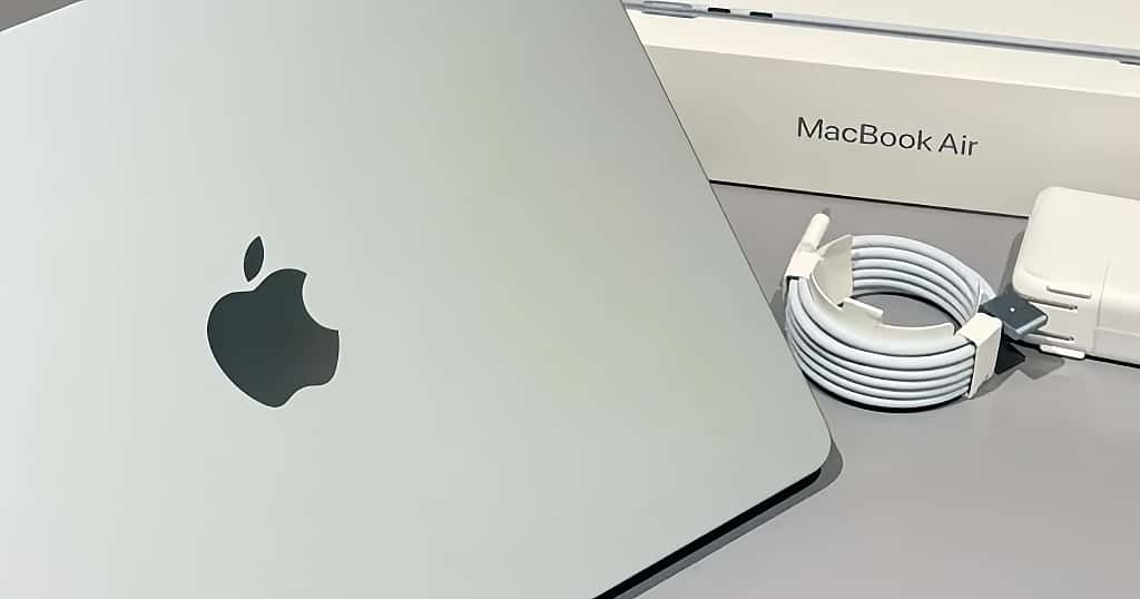 Laptop MacBook Air dengan logo Apple, adaptor daya, dan kabel pengisi daya di sebelahnya. Tentang memahami masa pakai baterai MacBook Air