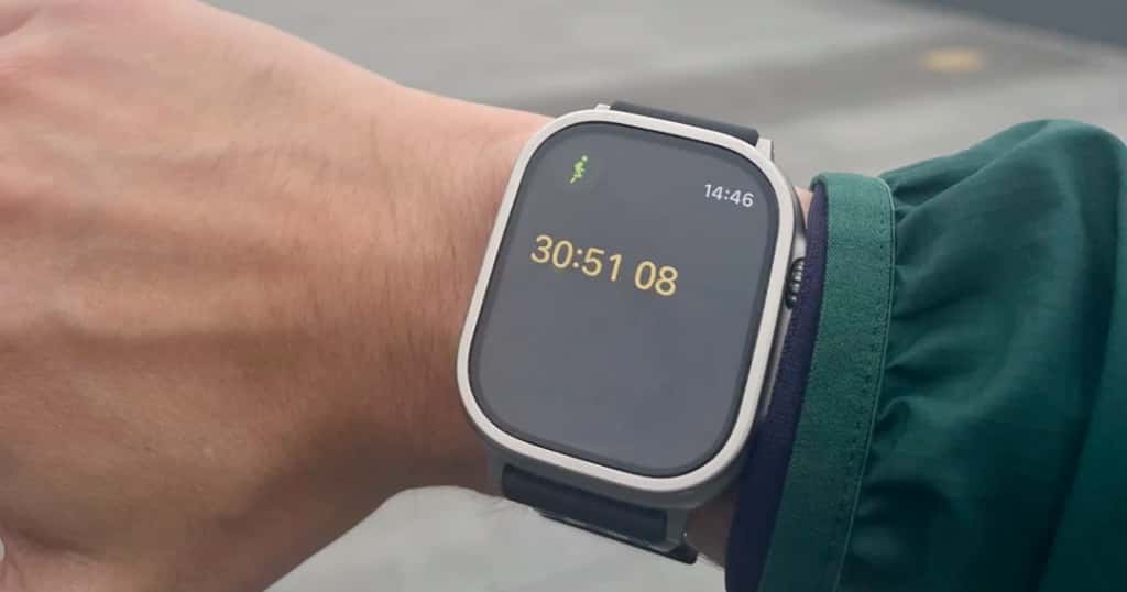 Apple Watch yang dikenakan di pergelangan tangan menampilkan antarmuka pengatur waktu lari, memamerkan kemampuan pelacakan waktu dan bantuannya kepada pelari