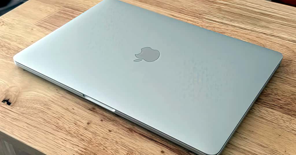 MacBook Pro berwarna perak di atas meja kayu, memperlihatkan panduan untuk memilih aksesori dan perlindungan yang tepat untuk setiap model