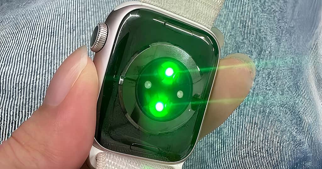 Sensor Apple Watch memancarkan cahaya hijau untuk memantau detak jantung menggunakan fotopletismografi (PPG), menunjukkan cara kerja pemantauan detak jantung optik