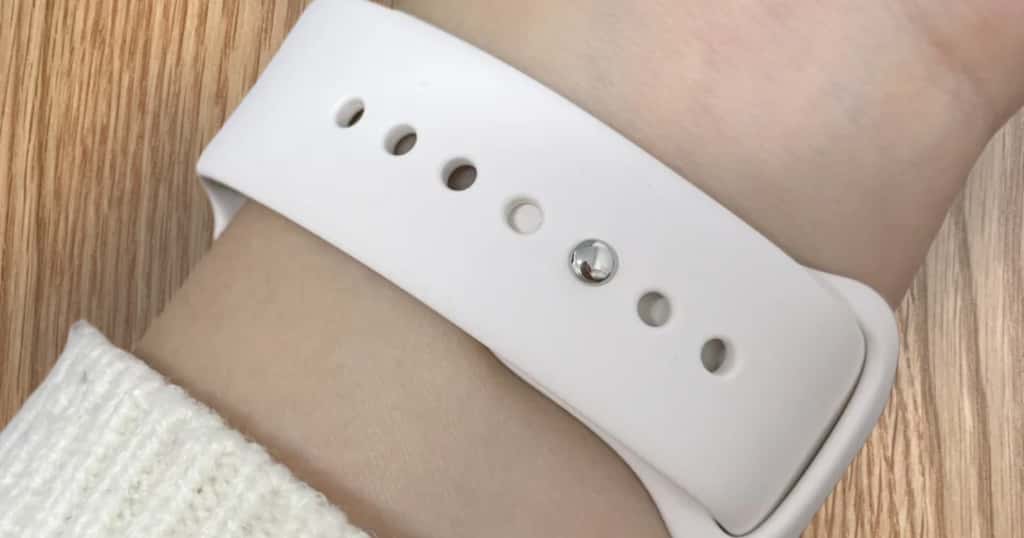 Közeli kép egy fehér sportszíjas Apple Watchról, amelyen látható a 44 mm-es modell illeszkedése és állíthatósága.