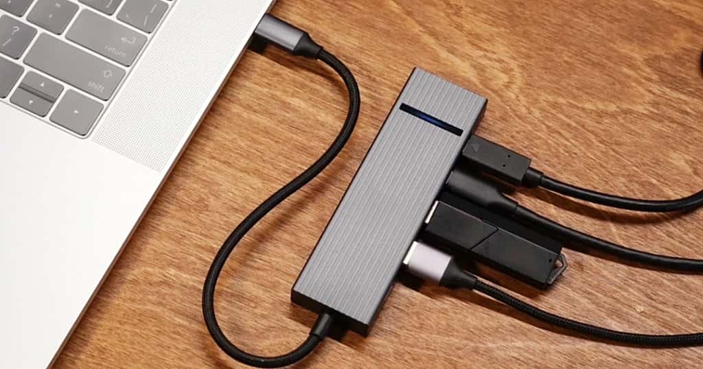 Una MacBook Air conectada a un adaptador USB-C multipuerto, colocada sobre una mesa de madera, que demuestra cómo ampliar la capacidad utilizando almacenamiento externo