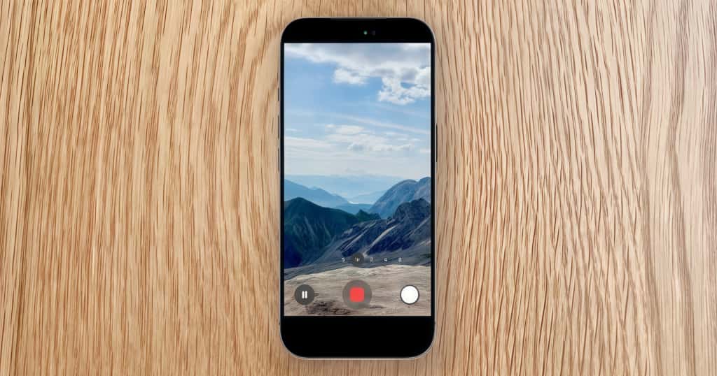 iPhone yang diletakkan di atas meja kayu memutar video pemandangan pegunungan, memamerkan fungsi anti-getaran kameranya untuk memastikan rekaman video halus dan jernih