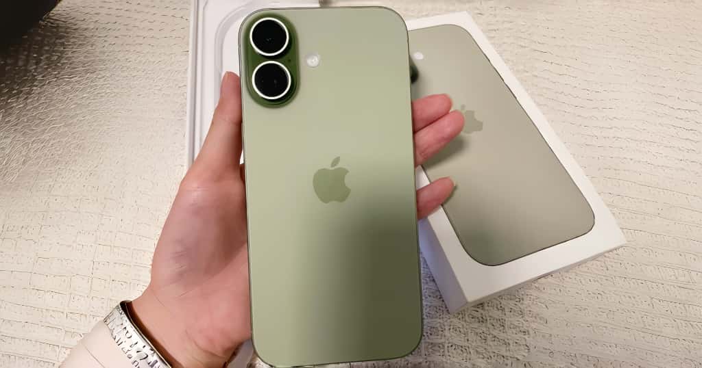 Sebuah iPhone hijau dipegang di satu tangan, dengan kotak telepon diletakkan di bawahnya, berfungsi sebagai demonstrasi kiat praktis untuk membeli iPhone bekas