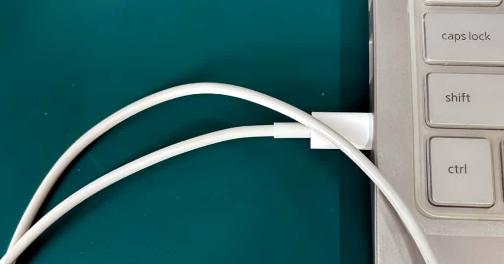 Kabel USB putih dihubungkan ke laptop, menunjukkan cara menghubungkan iPhone ke komputer melalui USB untuk berbagi koneksi jaringan