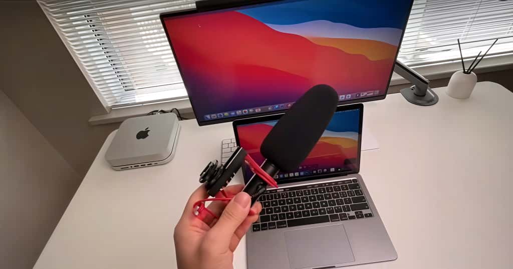 Grabar el sonido con un micrófono frente a un MacBook y un monitor externo, agregando audio a la grabación
