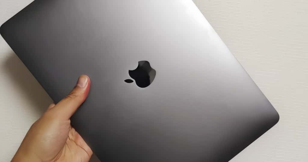 Sebuah tangan memegang MacBook Pro berwarna abu-abu, melambangkan alasan penting untuk memeriksa spesifikasi MacBook Pro