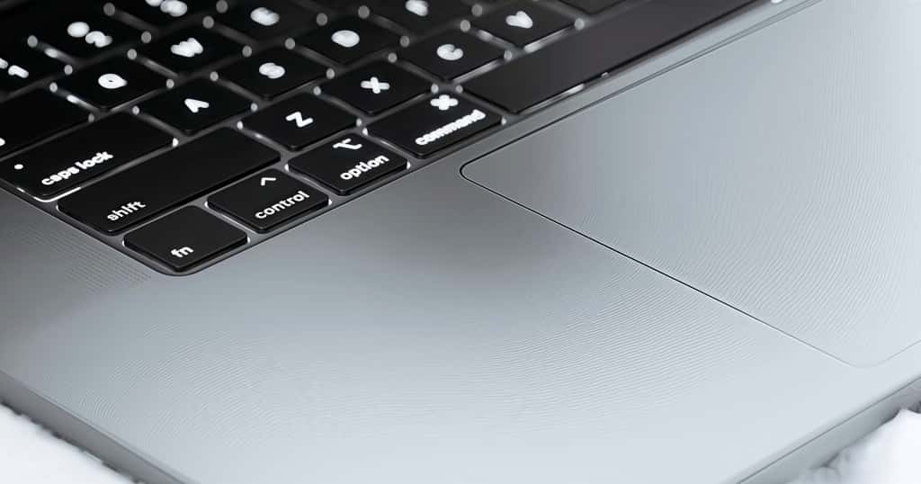 Tampilan dekat keyboard dan trackpad pada MacBook Pro abu-abu, mengilustrasikan langkah-langkah sederhana untuk memeriksa spesifikasi MacBook Pro Anda