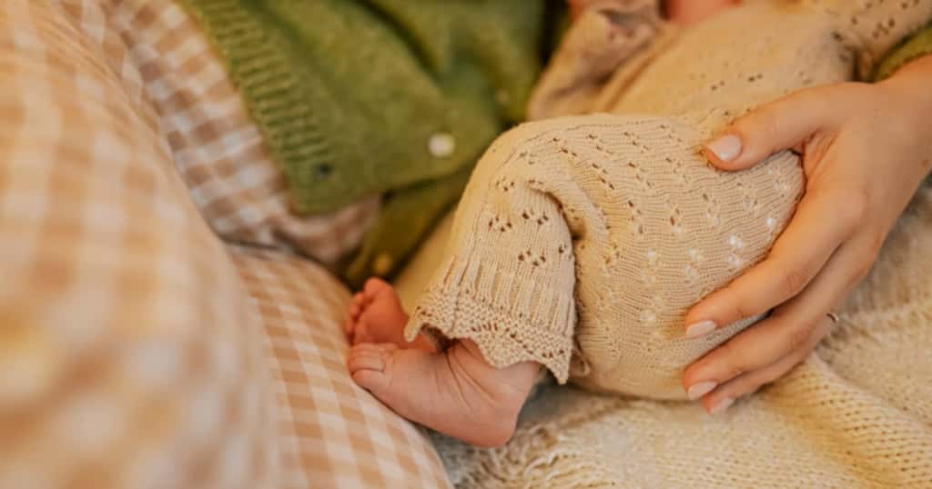Mutter liegt mit ihrem Baby im Bett und hält es ruhig im Arm